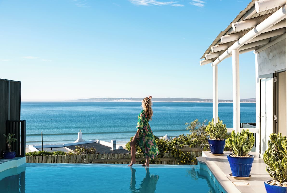 Una mujer con un vestido verde parada junto a una piscina con vista al océano.