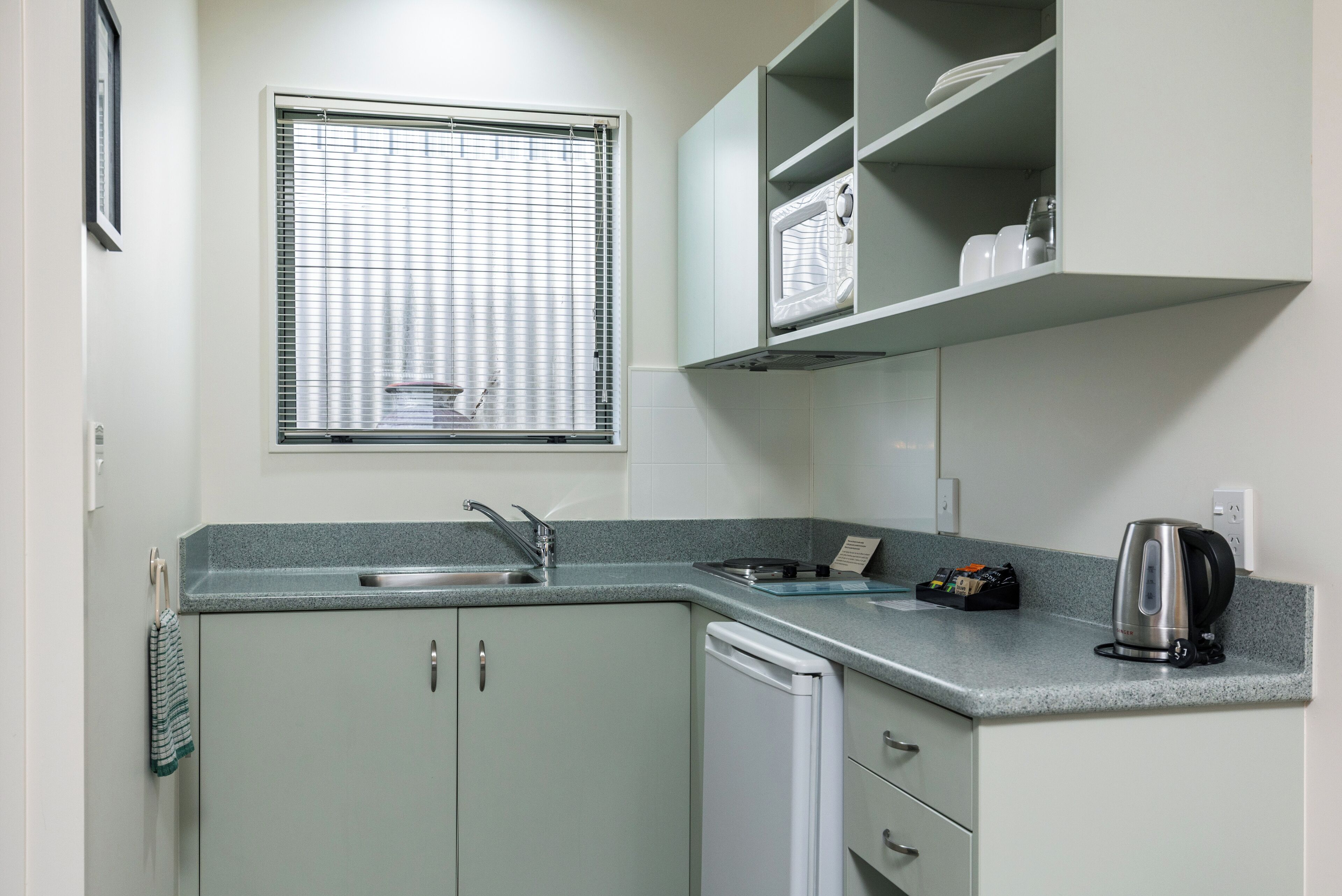 A kitchen with a built-in microwave, a kettle, and a sink.