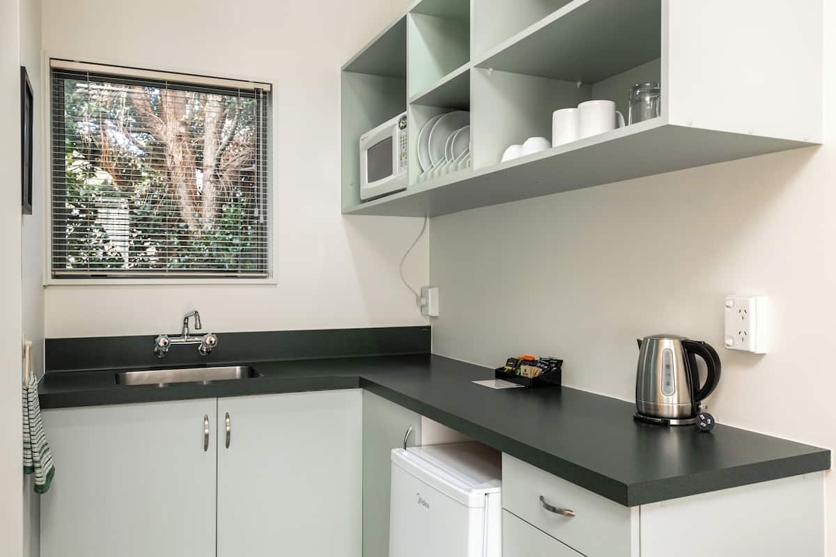 A kitchen with a black countertop, a built-in microwave, a kettle, and a small refrigerator.