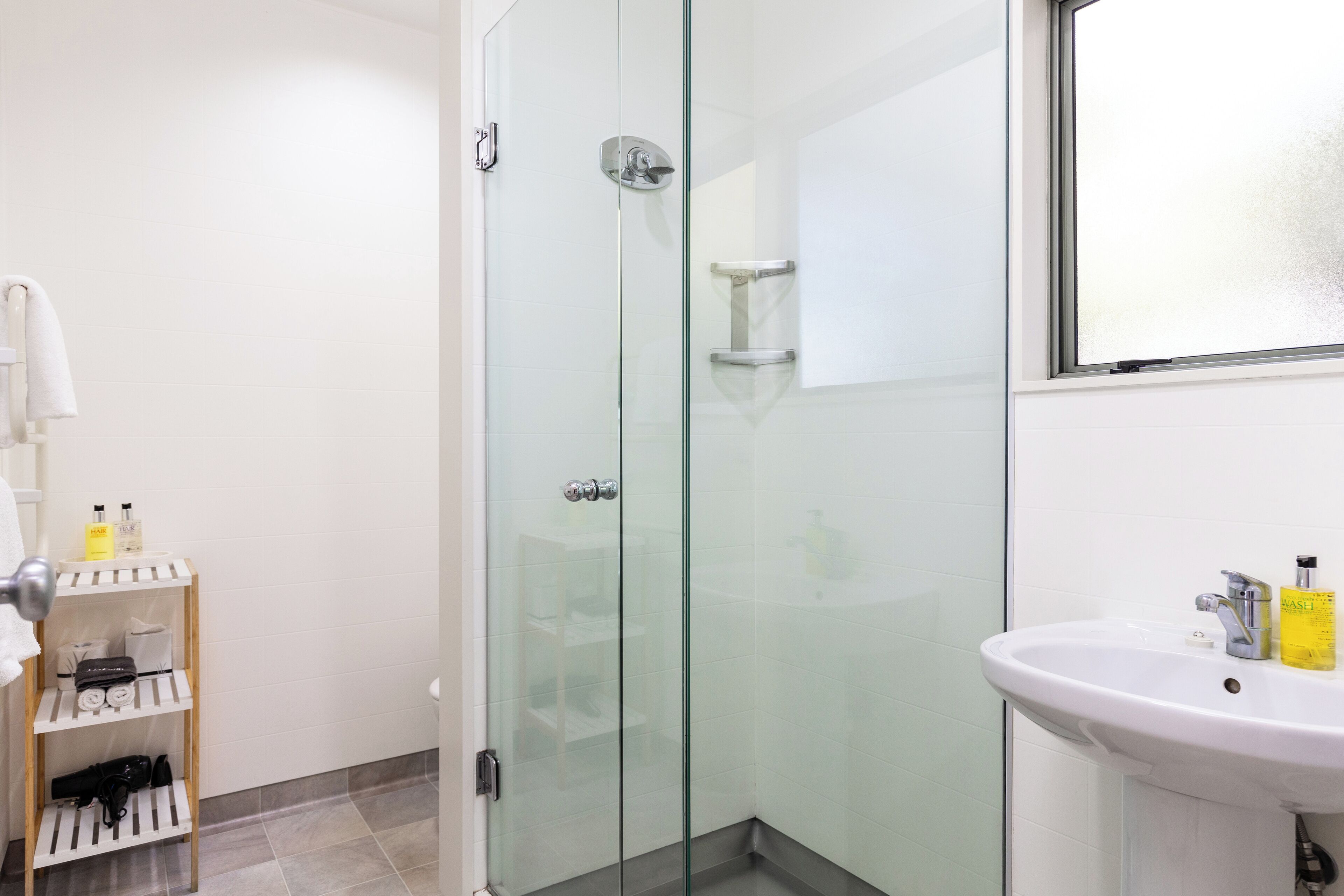 A modern bathroom with a glass-enclosed shower, a white sink, and a shelf with toiletries.