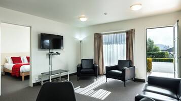 A hotel room with a bed, a TV, a desk, two chairs, and a large window with curtains.