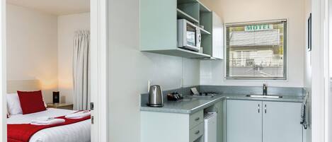 A compact hotel room with a bed, kitchenette, and a window with a view of the outside.