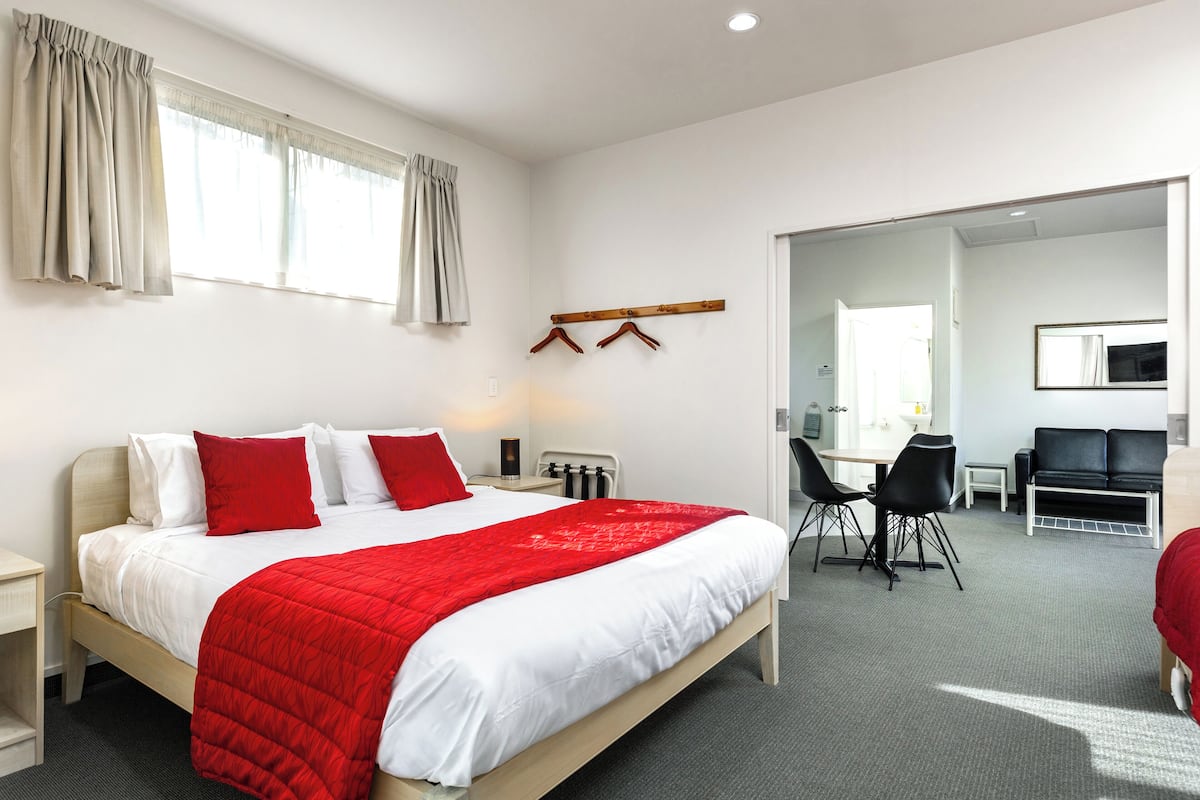 A hotel room with a large bed, a desk, a chair, a coat rack, and a mirror.