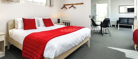A hotel room with a large bed, a desk, a chair, a coat rack, and a mirror.