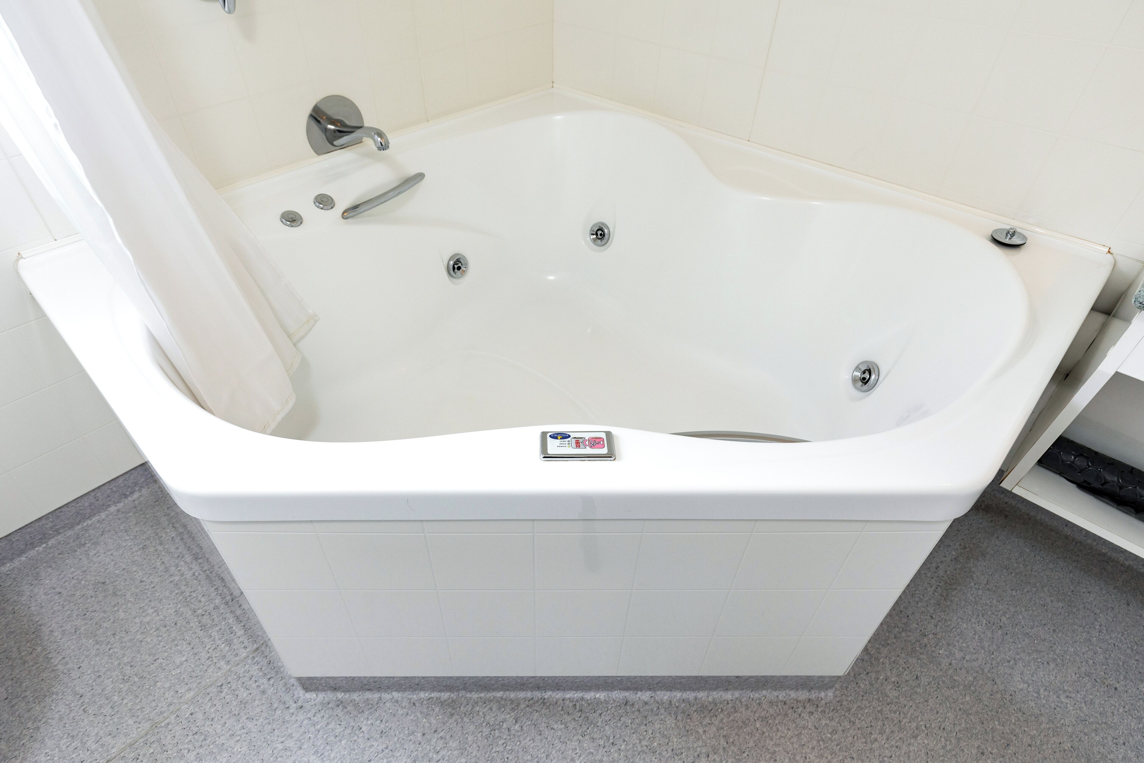 A white bathtub with a control panel, a showerhead, and a faucet.