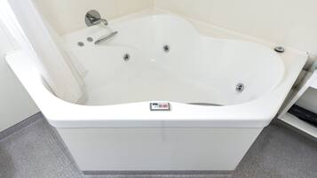 Una bañera blanca con un panel de control, un cabezal de ducha y un grifo.