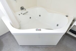 Una bañera blanca con un panel de control, un cabezal de ducha y un grifo.