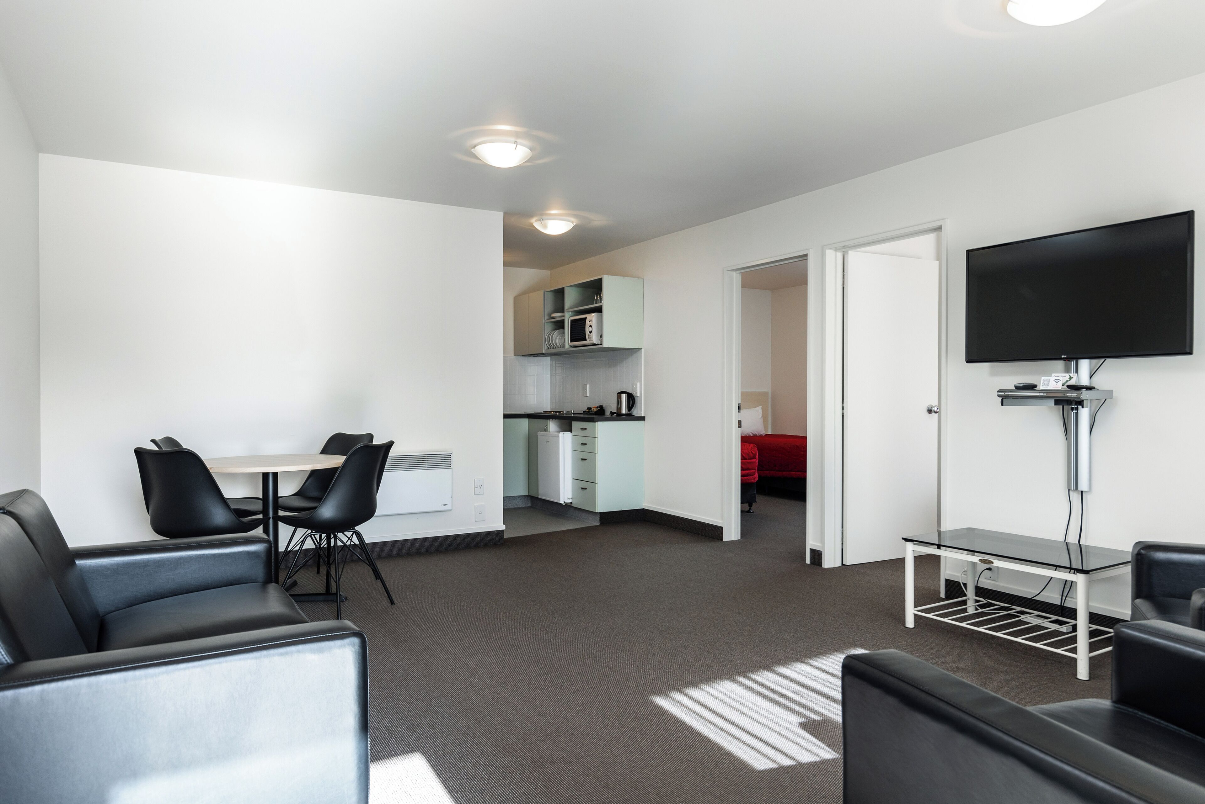 Una habitación de hotel moderna con comedor, kitchenette y televisor montado en la pared.
