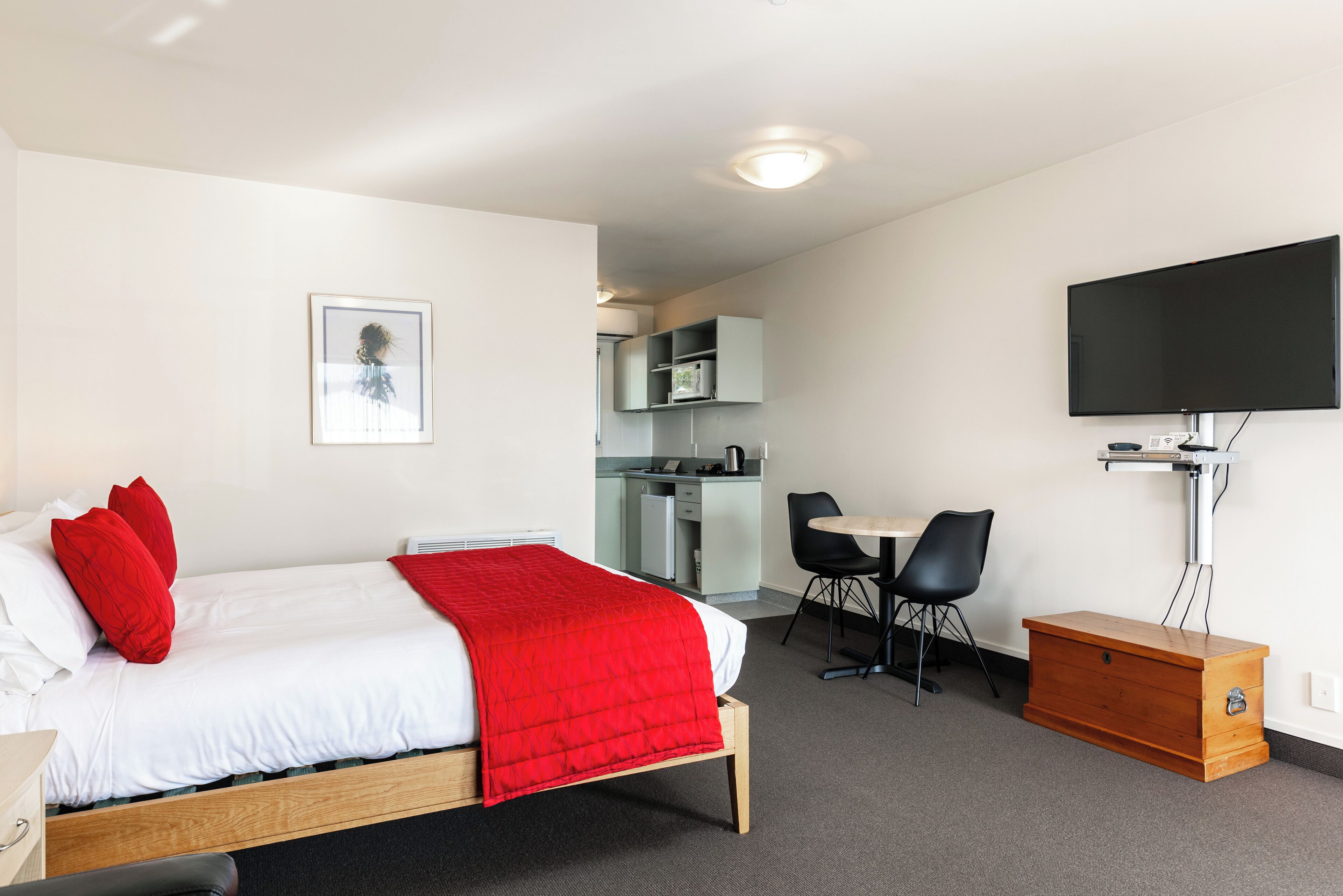 A hotel room with a bed, a desk, a chair, a television, and a kitchenette.