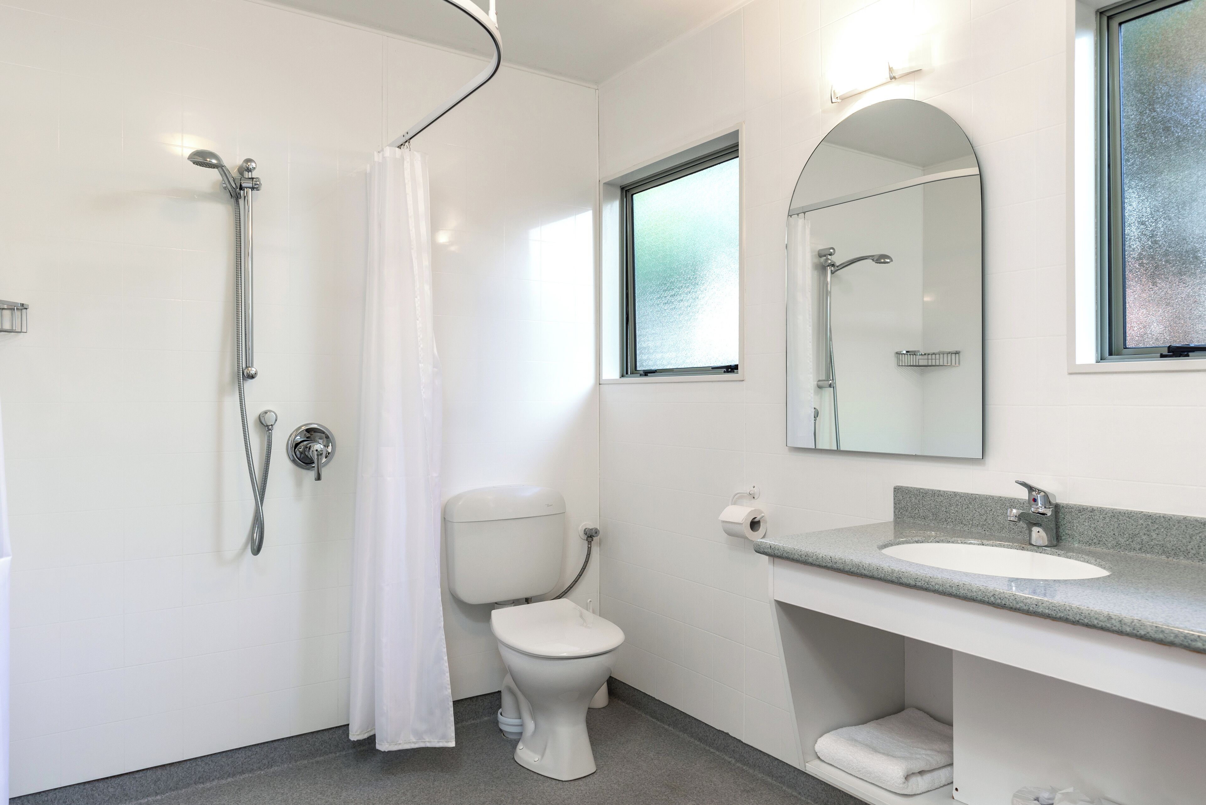 Un baño con ducha, inodoro, lavamanos y ventana.