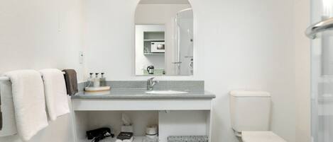 A modern bathroom with a white sink, a toilet, and a mirror above the sink. There are towels hanging on the wall and a trash bin under the sink.