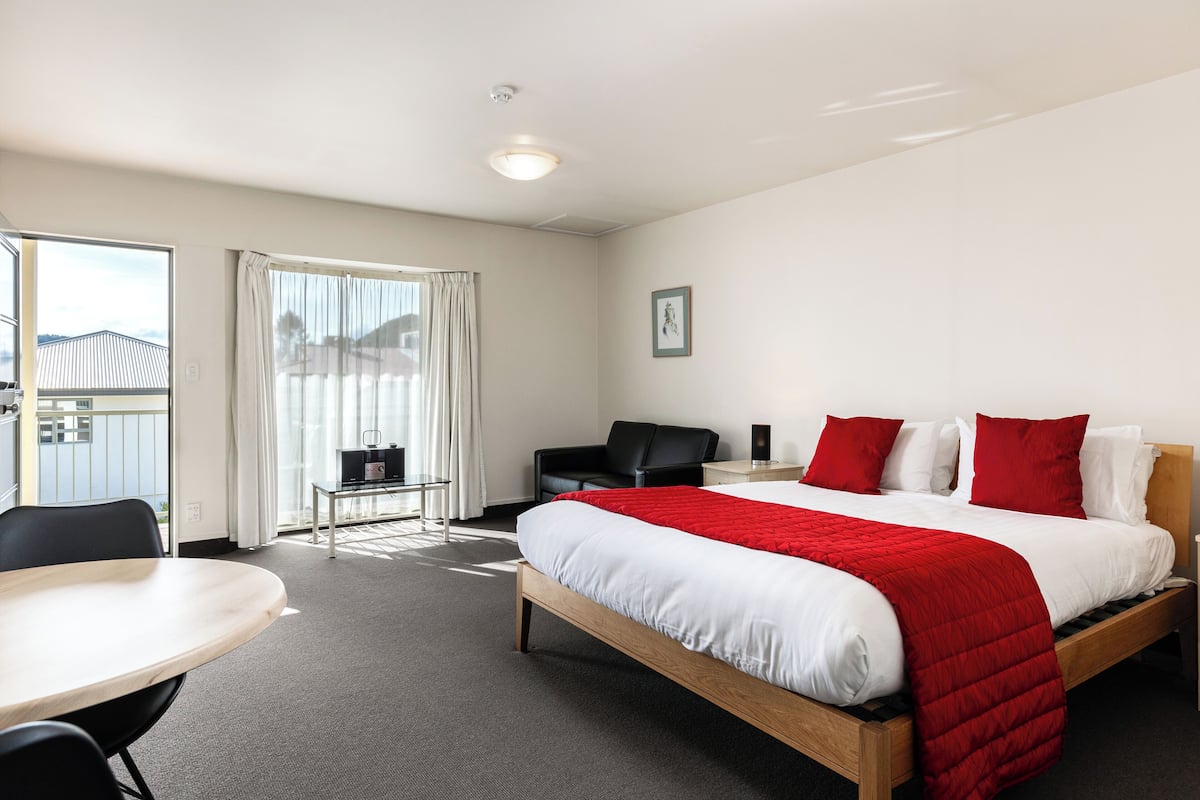 A hotel room with a bed, a desk, a chair, a small table, and a view of the outside.