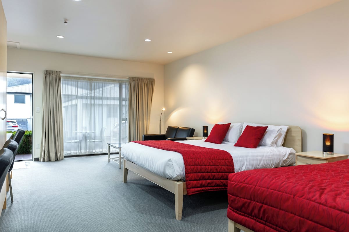 A hotel room with a large bed, a smaller bed, a desk, a chair, and a view of the outside.