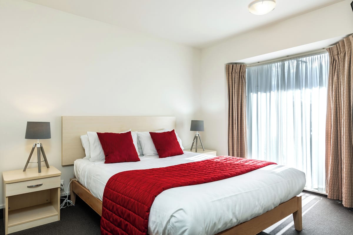 A hotel room with a large bed, two bedside tables, a lamp on each table, and a window with curtains.