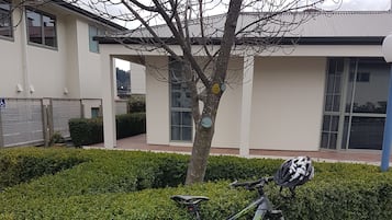 Un vélo est garé à côté d’une haie et d’un bâtiment doté de grandes fenêtres et d’un panneau indiquant qu’il est accessible aux personnes en fauteuil roulant.
