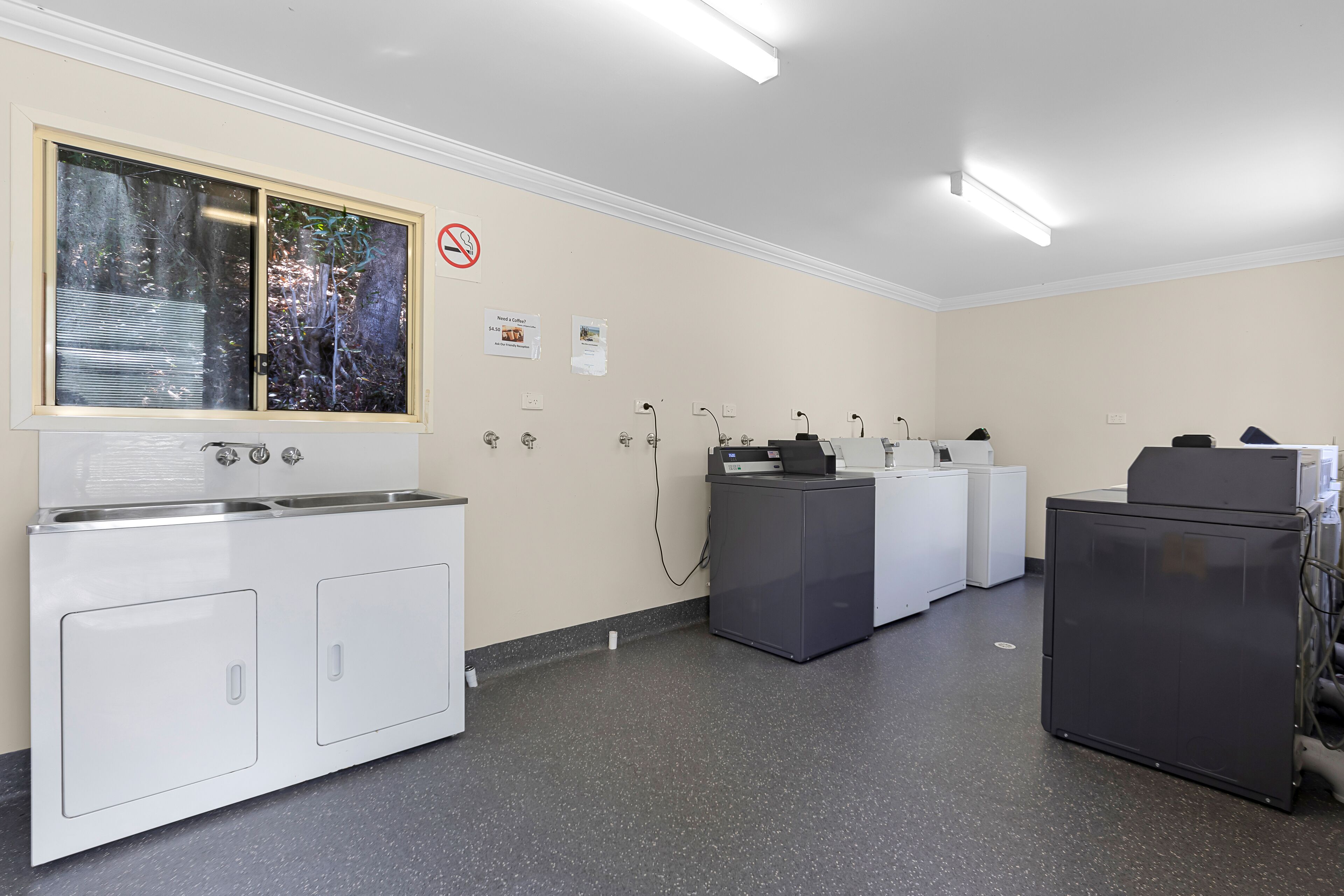 Una sala de lavandería con una lavadora industrial grande, una secadora y un cuarto de servicios con equipo eléctrico.