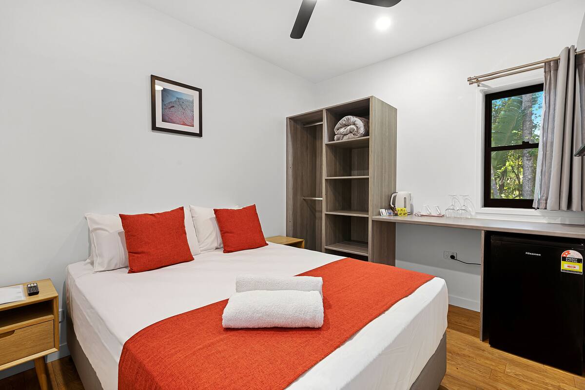 Une chambre d’hôtel avec un lit, un bureau, une armoire et une fenêtre avec des rideaux.