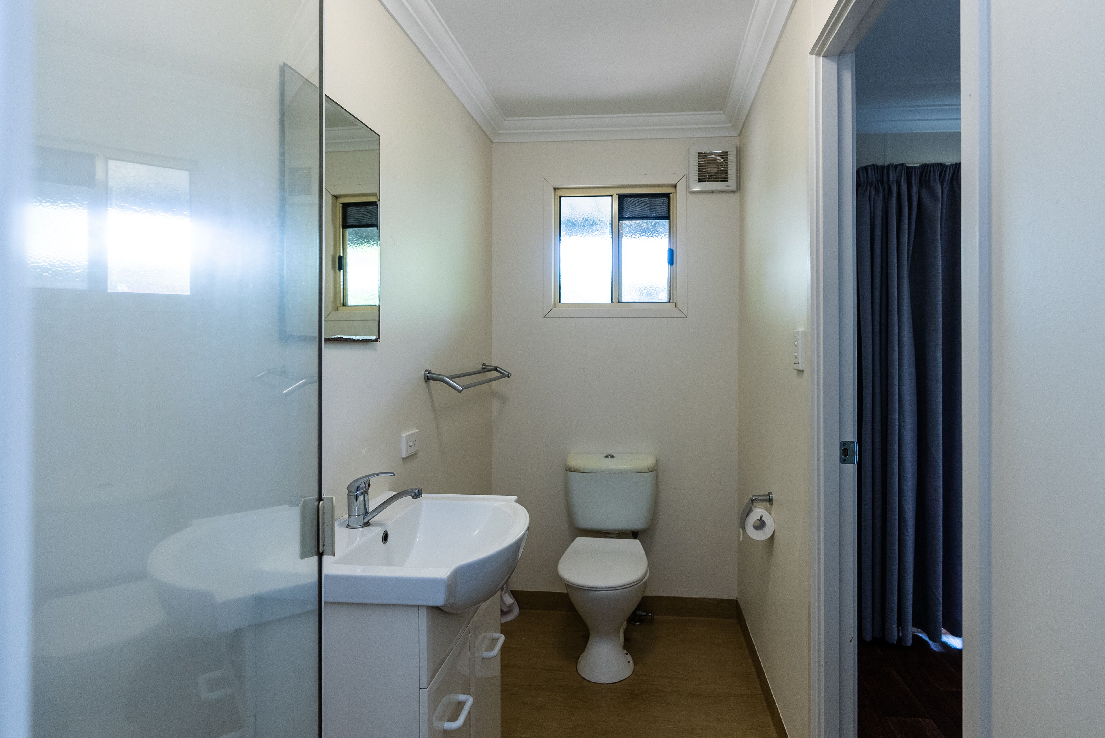 Un baño pequeño con un lavamanos blanco, un inodoro y un ventanal.
