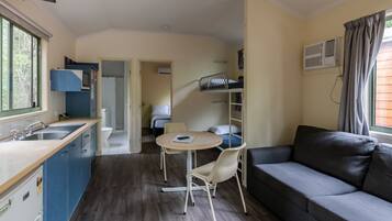 A compact room with a kitchenette, a sofa, a dining table with chairs, and a bunk bed.