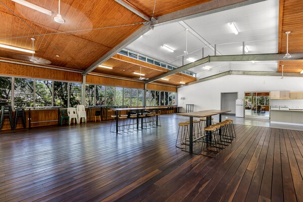 Un espacio interior amplio con techos altos, piso de madera y ventanas grandes que ofrecen vistas al exterior.