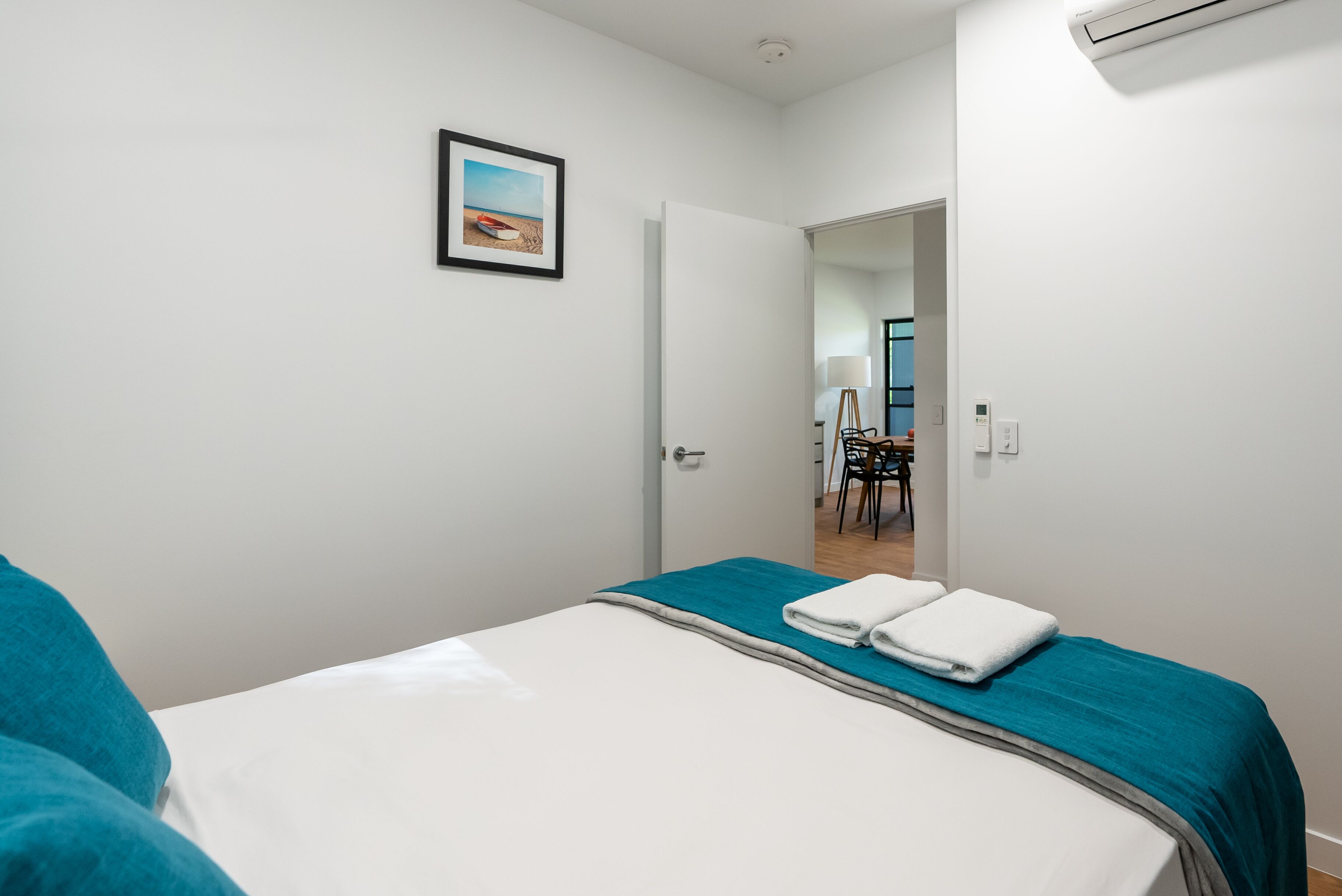 A hotel room with a bed, a door leading to a dining area, and an air conditioning unit.