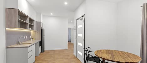 A modern kitchen with a wooden dining table and chairs, a built-in oven, and a refrigerator.