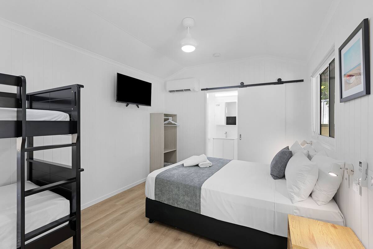 A modern bedroom with bunk beds, a flat-screen TV, a bedside table, and a mirror.