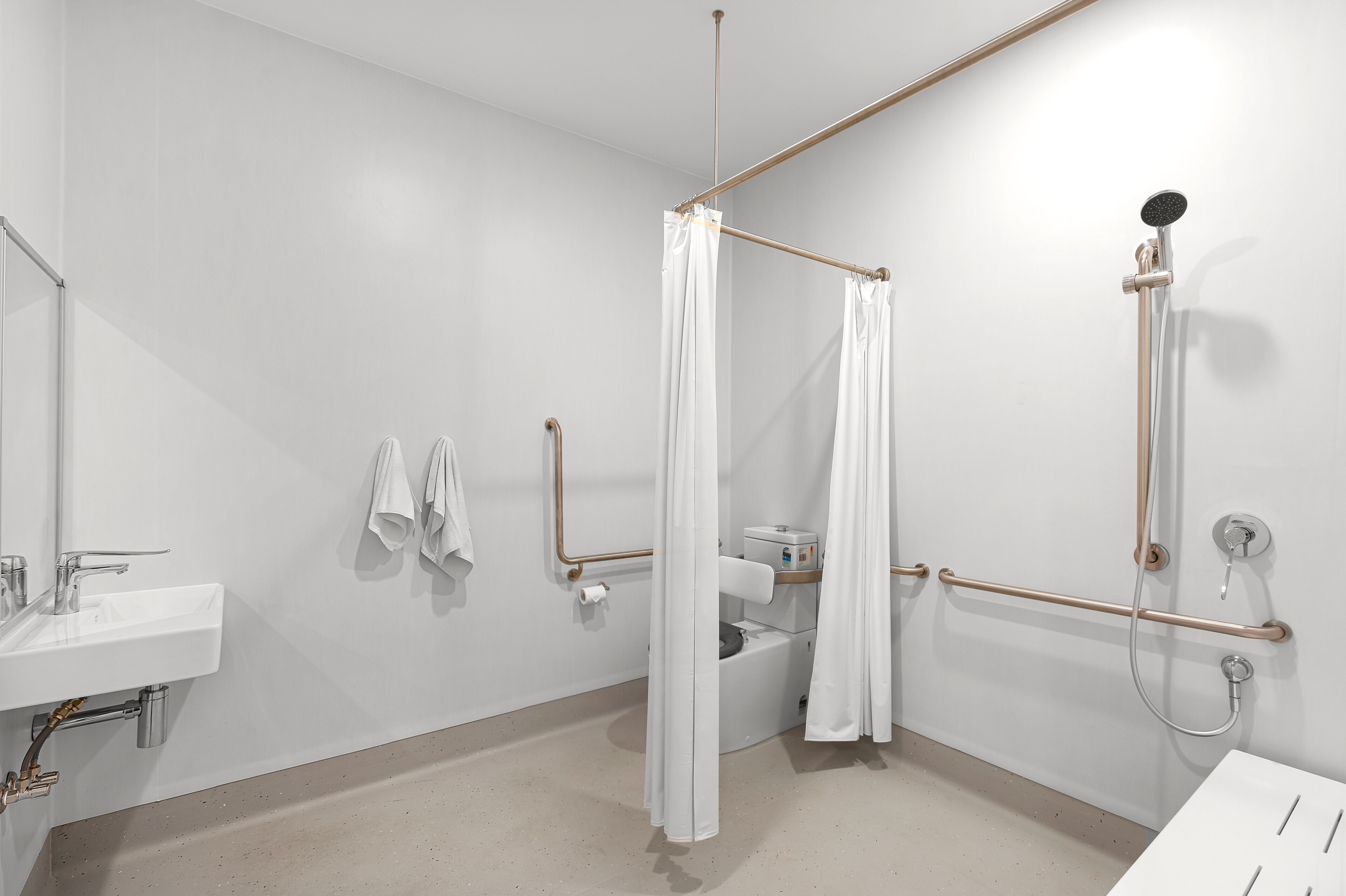 A modern bathroom with a white sink, a shower with a handheld showerhead, and a grab bar.
