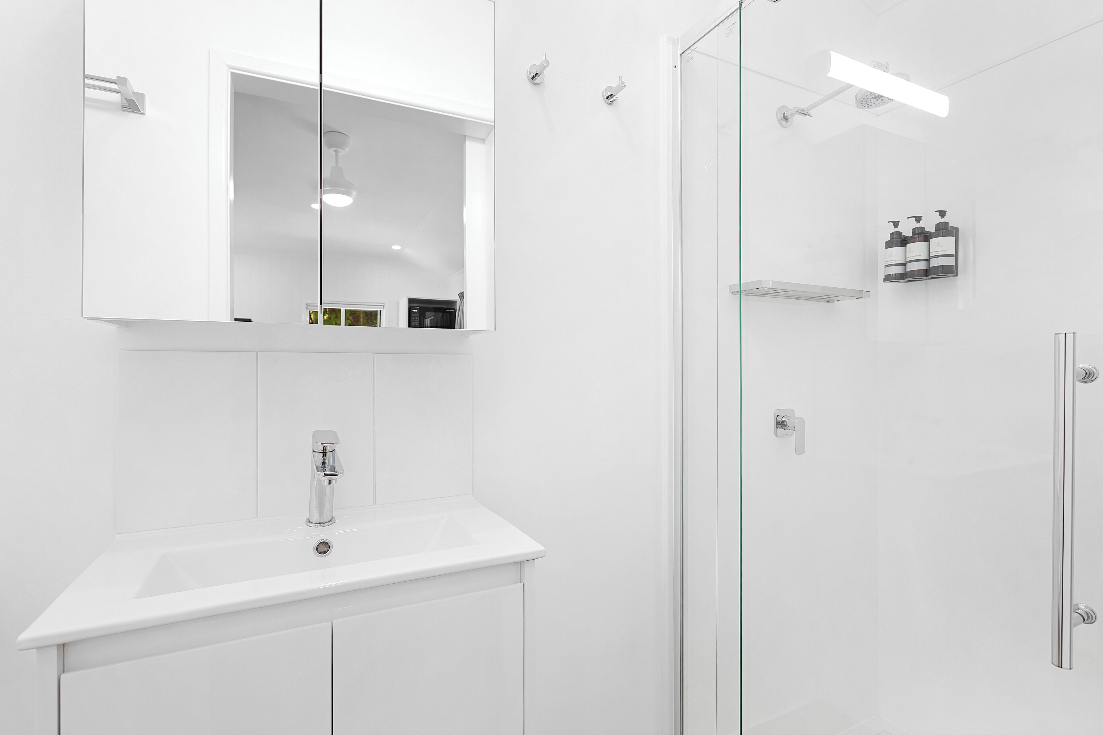 Un baño moderno con un lavamanos blanco, un espejo grande y una cabina de ducha de vidrio.