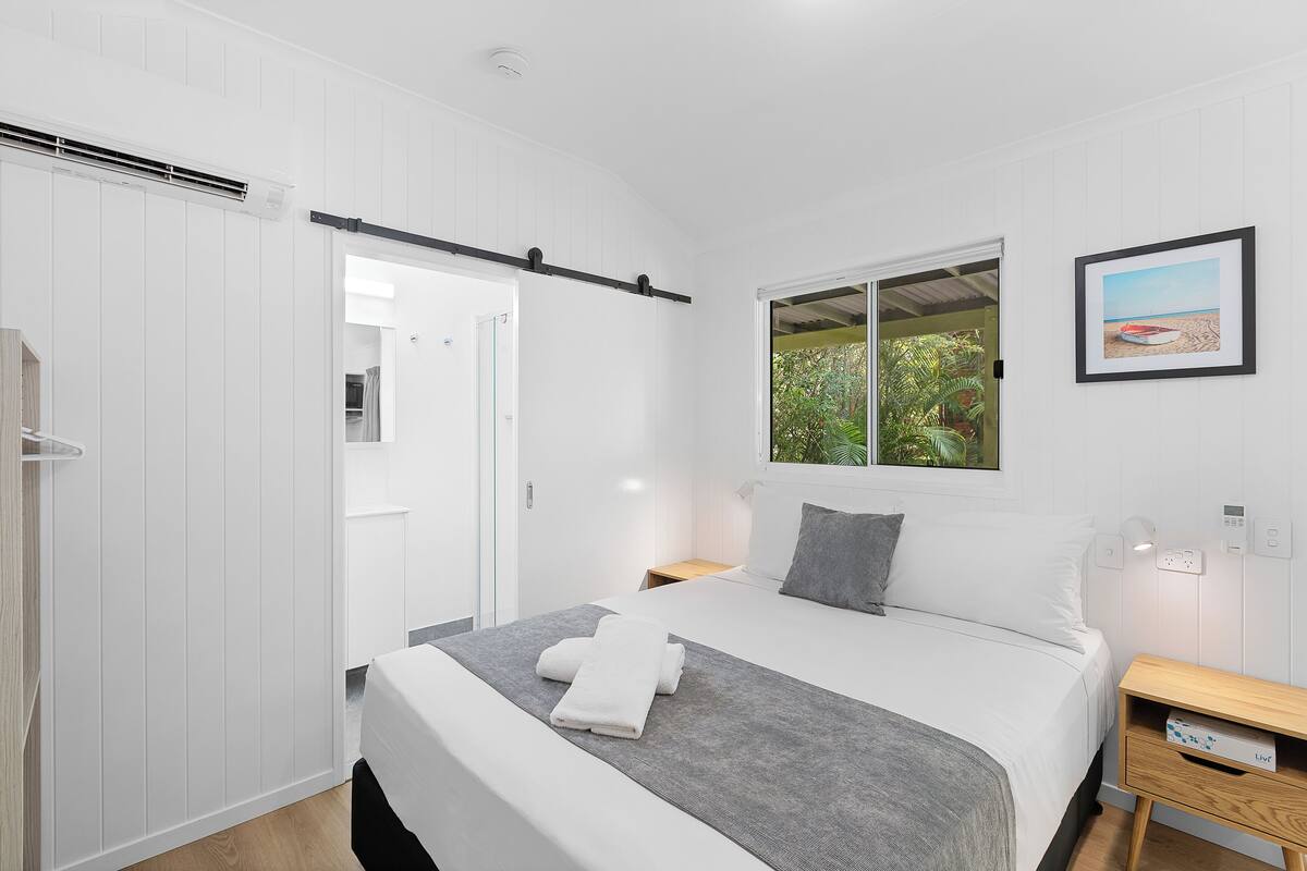 A bedroom with a bed, a bedside table, a nightstand, a window, and a door.