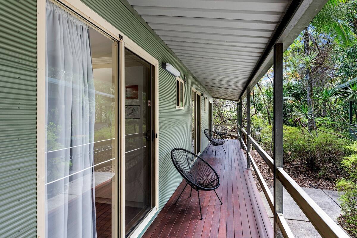 A covered porch with a wooden deck, sliding glass doors, and two black wire mesh chairs.