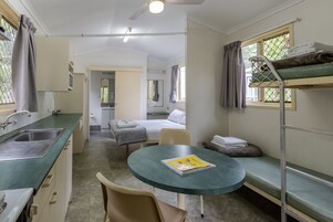A compact room with bunk beds, a small kitchenette, a round table, and a single chair.