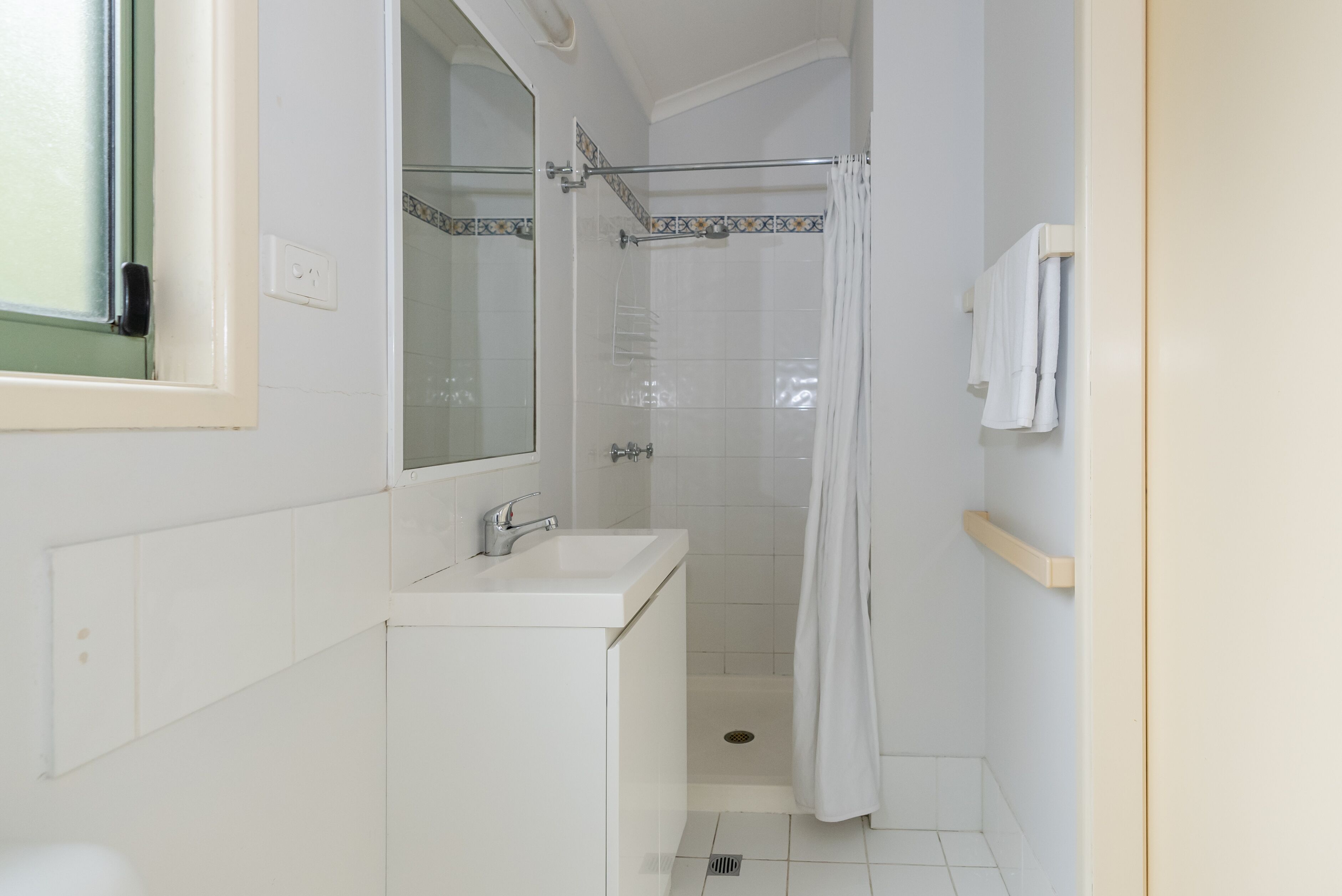 A small, clean bathroom with a white sink, mirror, and shower.