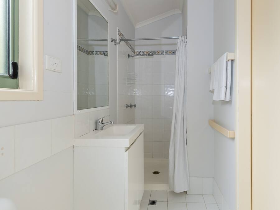 A small, clean bathroom with a white sink, mirror, and shower.