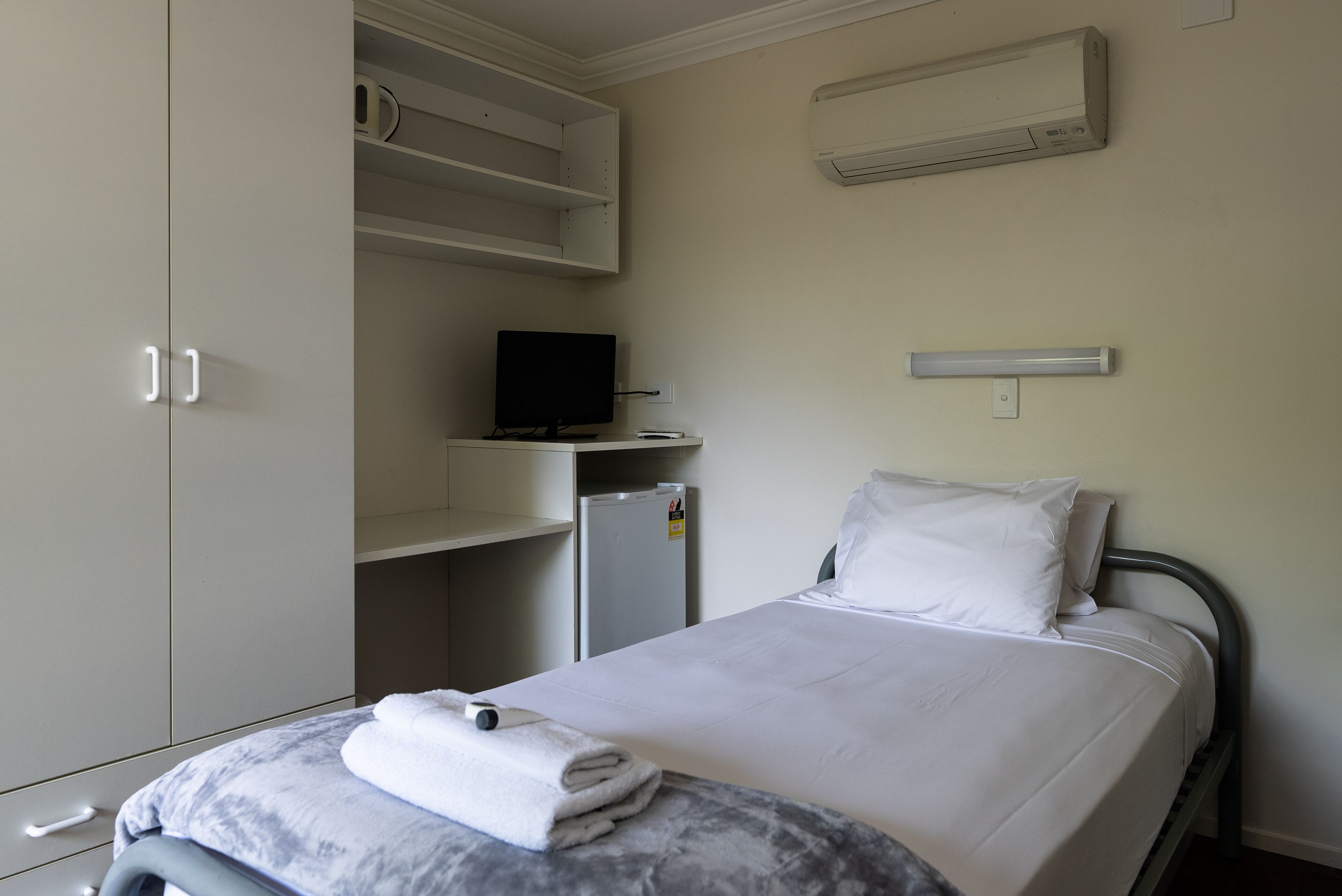 Quarto de hotel com cama, televisão, mini-frigorífico e armário.