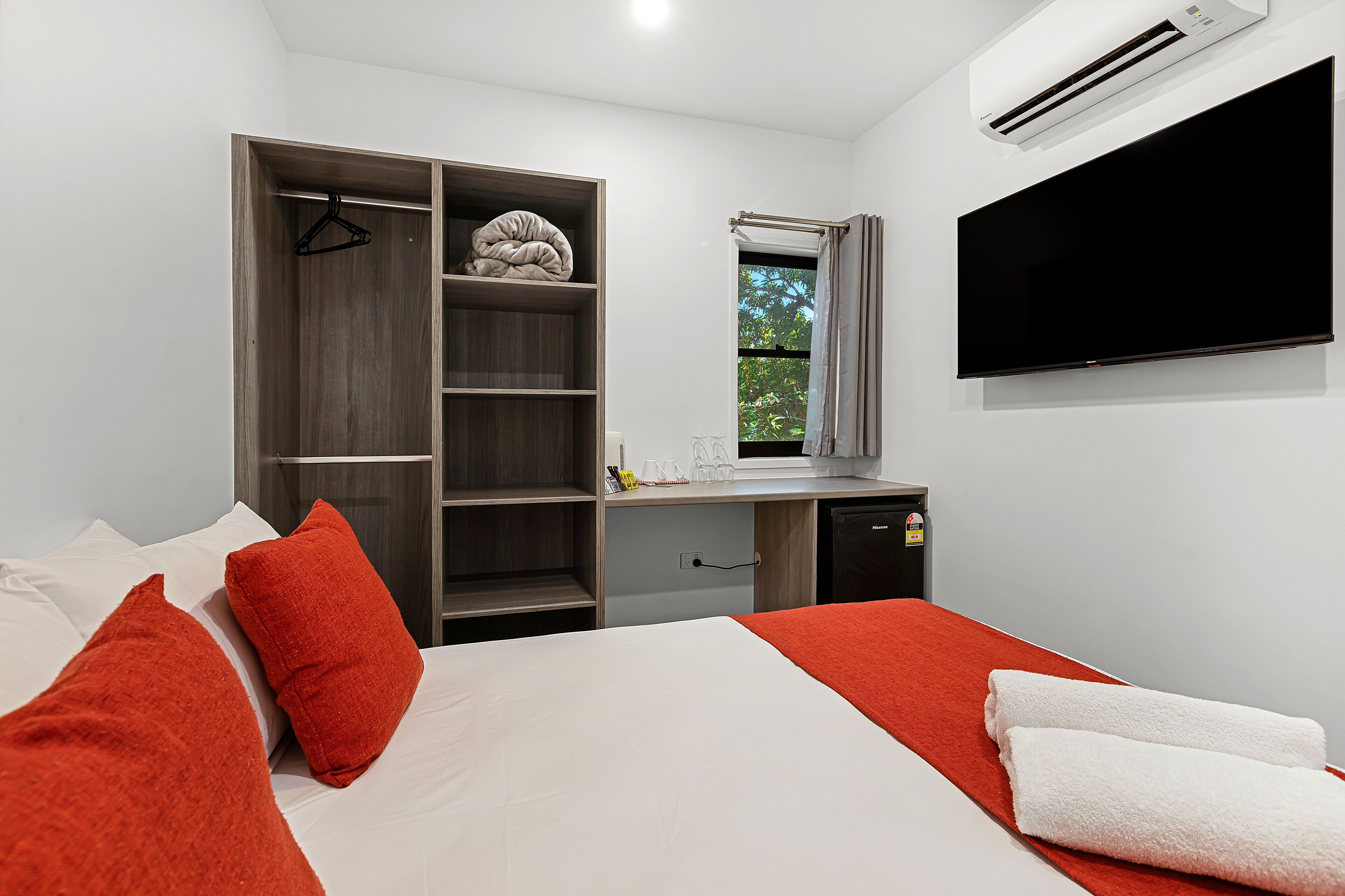 Un dormitorio con cama, armario, escritorio, televisor y aire acondicionado.