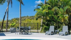 Un espace piscine agrémenté de chaises longues et d’une table, le tout entouré de grands palmiers.