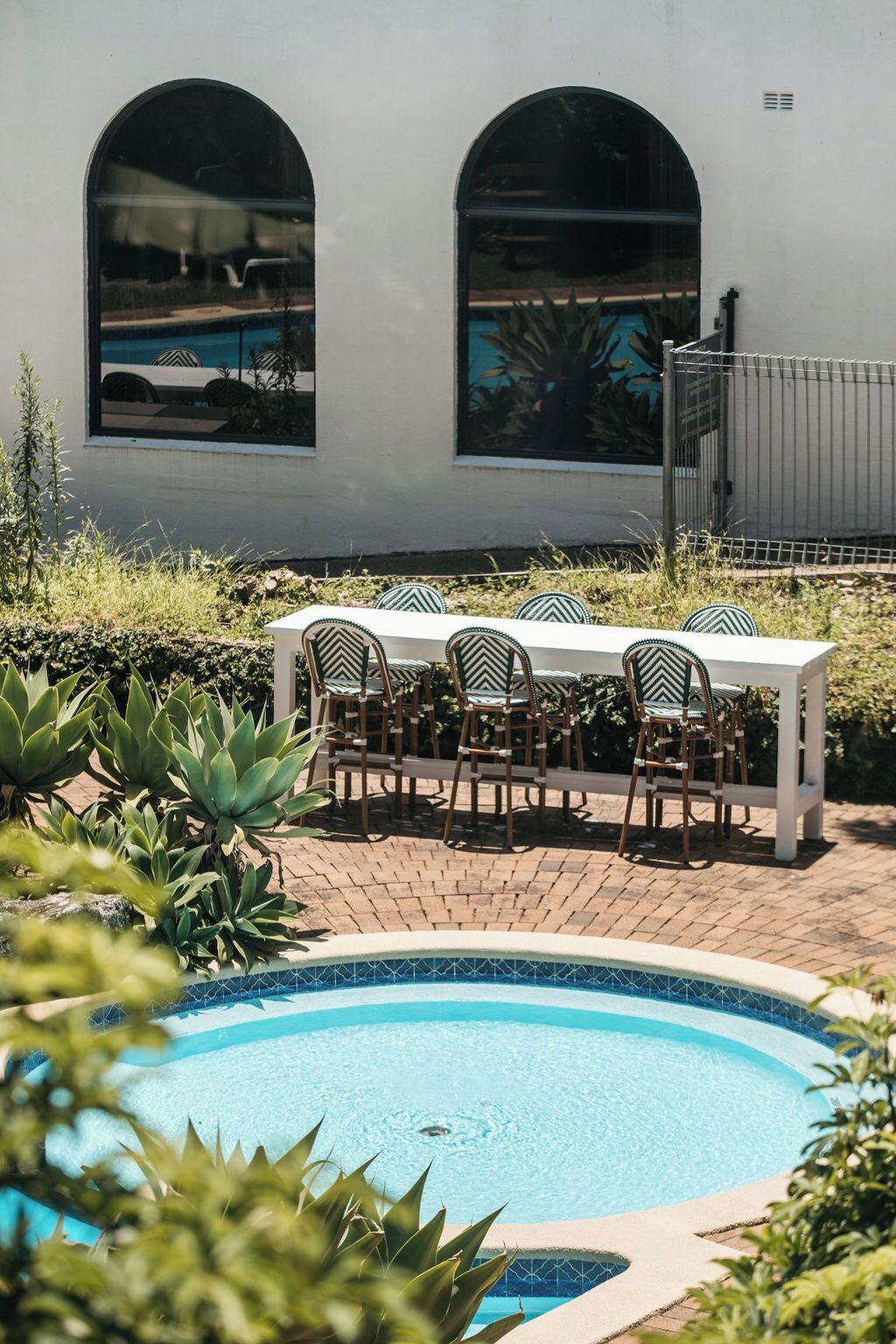 A poolside area with a table and chairs, a swimming pool, and a building with arched windows.