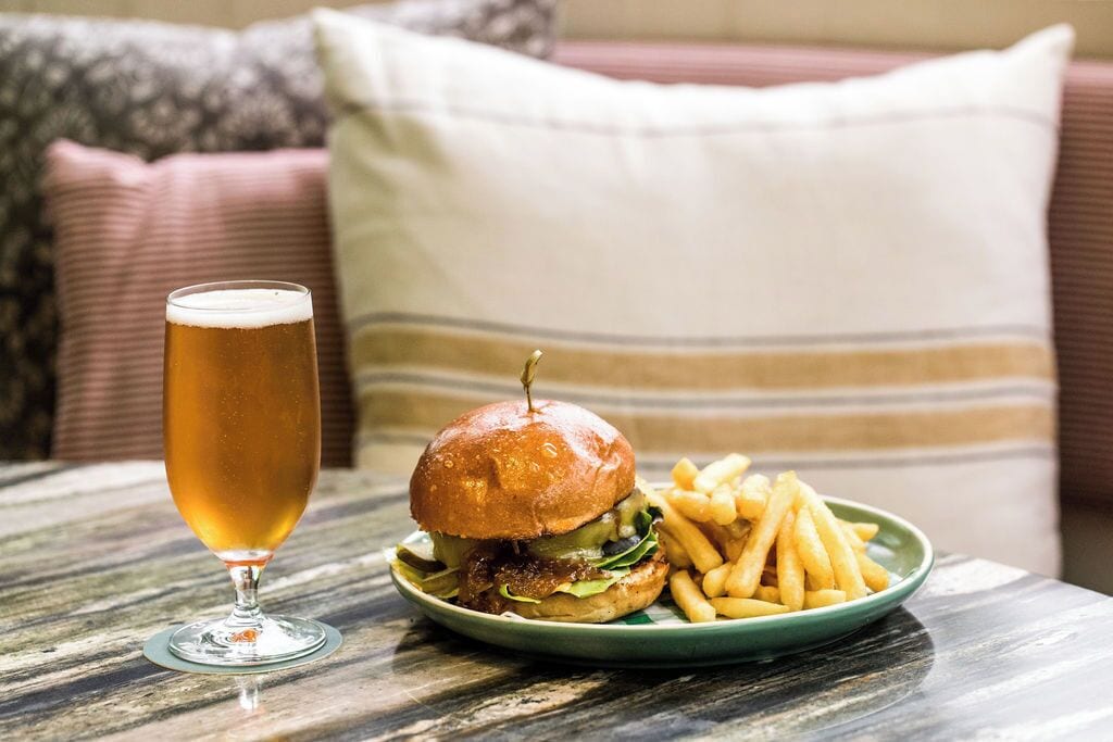 A meal consisting of a burger and fries on a plate, accompanied by a glass of beer, set on a wooden table.