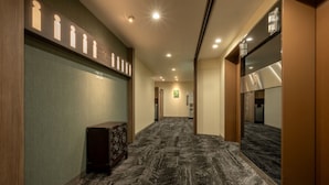 A hotel hallway with a carpeted floor, wooden paneling, a reception desk, and a mirrored wall. - Sendai Garden Palace (Sendai)
