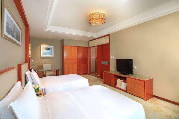Habitación de hotel con dos camas, televisión, escritorio y espejo.