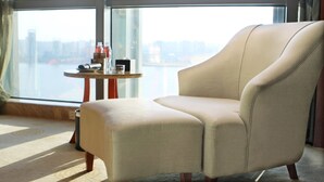 Una habitación moderna con un gran ventanal, un sillón acolchado, una mesita redonda y vistas a la ciudad.