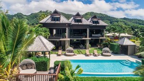 A large two-story house with a swimming pool, surrounded by lush greenery and palm trees. - Te Vakaroa Villas (Rarotonga)