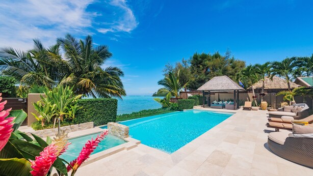 A swimming pool with a view of the sea, surrounded by palm trees and lounge chairs. - Te Vakaroa Villas (Rarotonga)