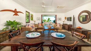 A spacious dining area with a large wooden table, wicker chairs, and a view of the outdoor patio. - Te Vakaroa Villas (Rarotonga)