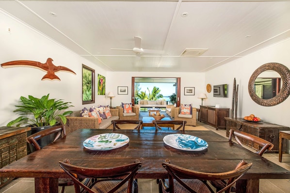 A spacious dining area with a large wooden table, wicker chairs, and a view of the outdoor patio. - Te Vakaroa Villas (Rarotonga)