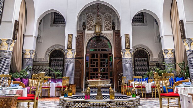 A multi-level interior with ornate arches, a central fountain, and a dining area with tables and chairs. - Riad El Yacout (Fes)