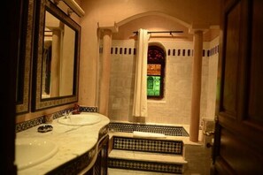A bathroom with two sinks, a large mirror, and a window with a stained glass design.