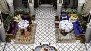 An indoor courtyard with two round tables, each surrounded by sofas and cushions, set on a patterned floor. - Riad El Yacout (Fes)