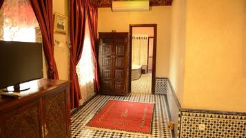 Un pasillo con piso a cuadros, un tapete rojo, un mueble de madera con un televisor y una puerta con intrincados grabados.